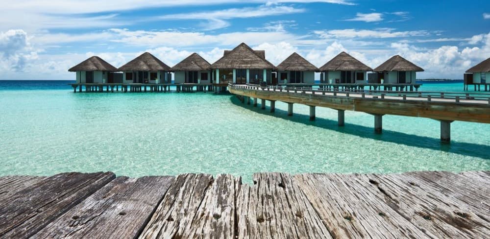 Overwater villas scattered across a turquoise Maldivian atoll seen from above
