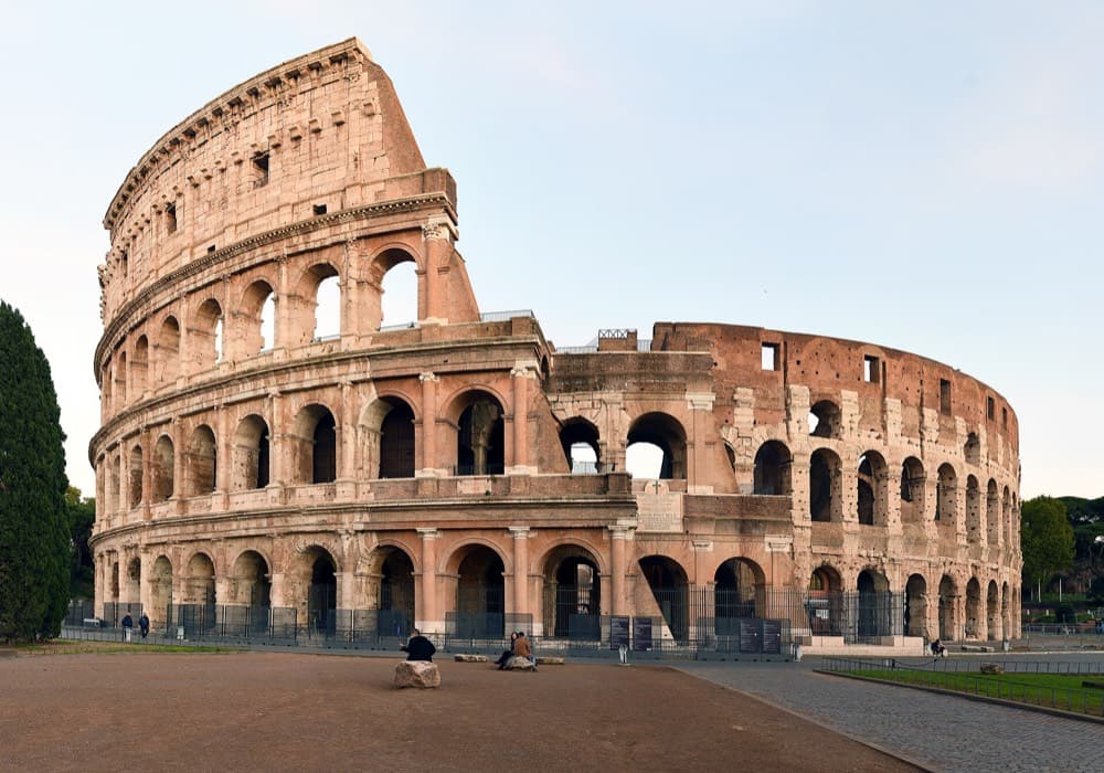 The Colosseum and Roman Forum lit warmly against the city skyline at dusk
